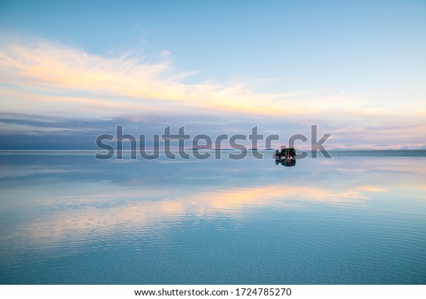 \
UYUNI SALT FLAT /\
BOLIVIA - APRIL 18, 2019: а car with people is in the water in\
which the sky is\
reflected.