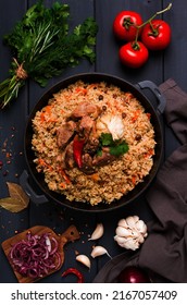 Uzbek pilaf, stewed rice with meat, in a cast-iron cauldron, on a dark gray wooden table, top view, no people, toned, - Shutterstock ID 2167057409
