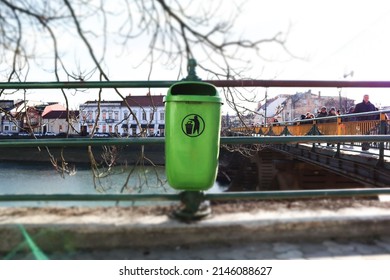 Uzhgorod, Ukraine. March 1, 2021. A Green Trash Can Outdoors In An Urban Environment. Garbage Can On A City Street. Rubbish Bin On A Walkway On A River Bank With Tilt-shift Effect Garbage Dumping Site