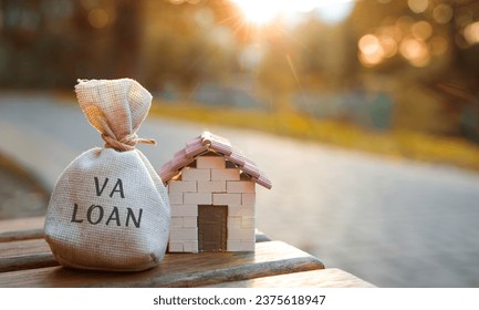 Va loan concept - government-backed mortgage option available to Veterans, service members and surviving spouses. Money bag and miniature house in the park in the sunset light. Real estate and finance