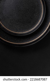 Vacant black ceramic dinner plate. The background is black leather. Luxurious, sumptuous fine tableware.Flat lay, top view, vertical photo - Shutterstock ID 2218687087