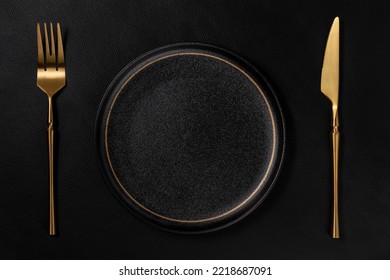 Vacant black ceramic dinner plate. The golden tableware is placed on the background is black leather. Luxurious, sumptuous fine tableware.Flat lay, top view, banner,horizontal photo