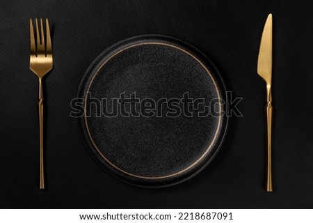 Vacant black ceramic dinner plate. The golden tableware is placed on the background is black leather. Luxurious, sumptuous fine tableware.Flat lay, top view, banner,horizontal photo