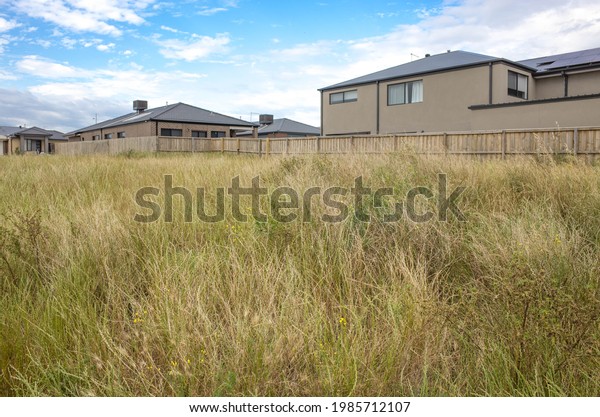 Vacant land\
block covered with long grass, some modern residential houses in\
the background. Concept of real estate development, and land for\
sale. Tarneit, Melbourne, VIC\
Australia.