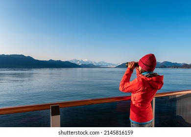 Vacation adventure. Alaska Glacier Bay cruise ship passenger looking at Alaskan mountains with binoculars exploring Glacier Bay National Park, USA. Woman on travel Inside Passage enjoying view