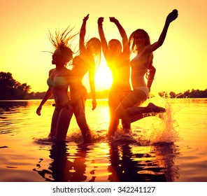 Vacation. Beach Party. Teenage Girls Having Fun In Water. Group Of Happy Young People Dancing At The Beach On Beautiful Summer Sunset. Silhouettes Of Group Of Teen Girls Jumping. Joyful Friends