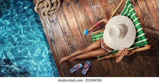 Vacation. Beautiful young woman relaxing on beach chair with cocktail. Top view