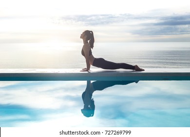 Vacation of Calm Attractive Asian woman practice yoga Cobra Pose on the pool above beach in the morning with beautiful sea in Tropical island,comfortable and relax in holiday.Yoga Vacations Concept