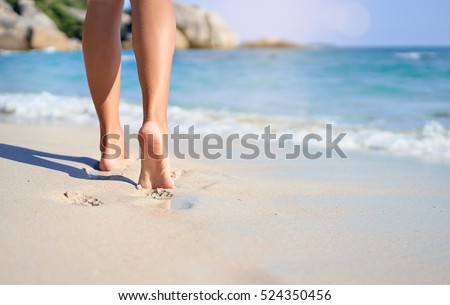Vacation concept. Close up of female legs walking by the beach.