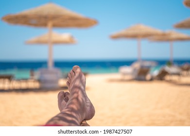 Vacation Concept. Man's Bare Feet Over Sea Background. Man Tanned Legs On Sand Beach. Travel Concept. Happy Feet In Tropical Paradise. Feet On Beach, Summer Holiday Concept.