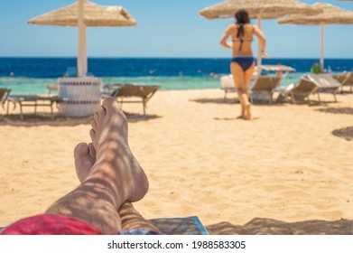 Vacation Concept. Man's Bare Feet Over Sea Background. Man Tanned Legs On Sand Beach. Travel Concept. Happy Feet In Tropical Paradise. Feet On Beach, Summer Holiday Concept.