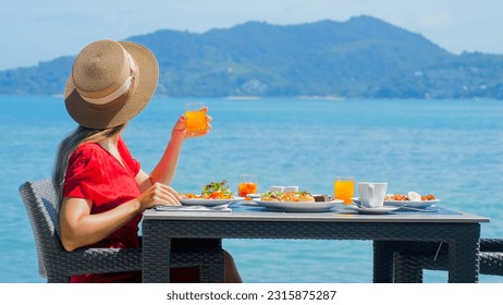 Vacation girl in luxury resort enjoys morning breakfast with fresh food and tropical sea view. Happy young woman on beachfront dining. Travel, vacation, summer holidays concept - Powered by Shutterstock