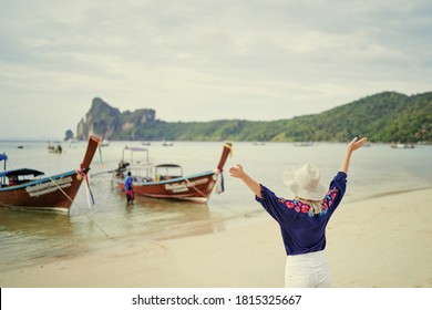 Vacation and happiness. Woman in hat rising hands up standing on tropical beach with beautiful view in Thailand.