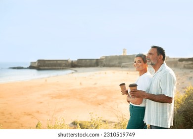 Vacation. Happy Senior Travelers Couple With Coffee Cups Posing At Ocean Outdoor, Drinking Hot Drinks And Enjoying Day At Seaside. Side View Shot Of Loving Spouses Near Sea. Free Space For Text - Shutterstock ID 2310519749