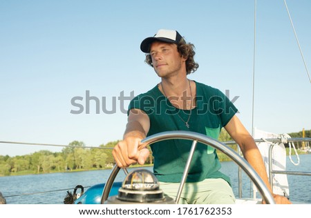 Vacation, holidays, travel, sea and people concept - young man i steering wheel and looking far away on yacht on lake.