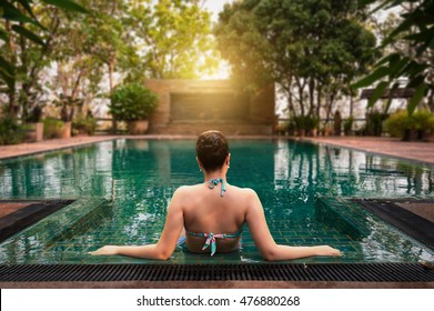 Vacation lifestyle scene of young woman sitting in swimming pool in morning time. Weekend and holiday lifestyle concept