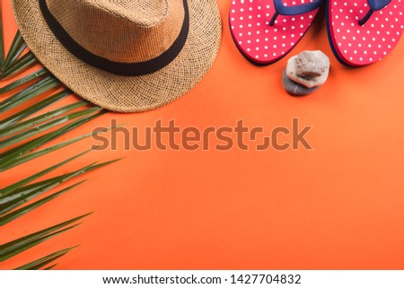 Vacation on the beach. Flat lay on orange coral background. Fern, hat, flip flops, stones.