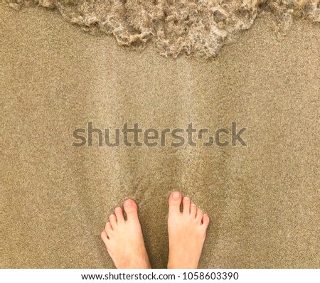 Vacation on ocean beach, female feet on sea sand,  with a wave's edge. Beach travel - woman stands on sand beach