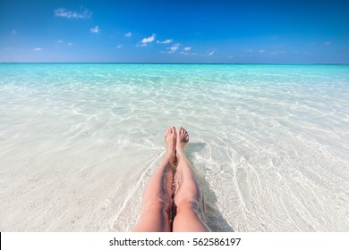 Vacation on tropical beach in Maldives. Woman's legs in the clear ocean water. First person perspective - Powered by Shutterstock