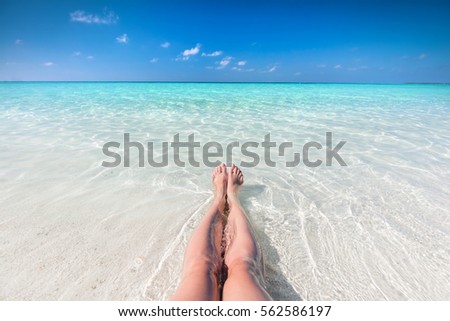 Vacation on tropical beach in Maldives. Woman's legs in the clear ocean water. First person perspective