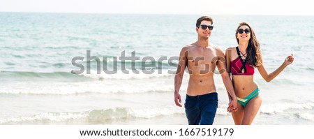 Vacation romantic lovers young happy couple holding hands walking on sand by sea having fun and relaxing together with copy space banner for adding text on tropical beach.Summer vacations and travel