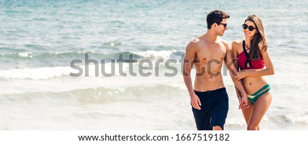 Vacation romantic lovers young happy couple holding hands walking on sand by sea having fun and relaxing together with copy space banner for adding text on tropical beach.Summer vacations and travel