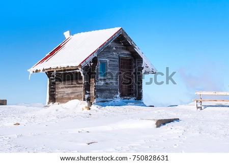 Vacation rural winter background with small wooden alpine house covered with snow, snow field, blue sky, copy space
