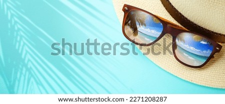 vacation and summer travel banner concept on tropical sea. Panama hat and sunglasses with a reflection of the sandy trovic beach and palm trees;
