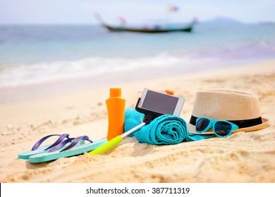 Vacation and technology. Must have accessories on the sea beach. Smartphone, selfie stick, hat, towel and sunglasses. - Powered by Shutterstock