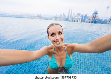 Vacation And Technology. Pretty Young Woman Taking Selfie While Swimming In Roof Top Pool With Beautiful City View.