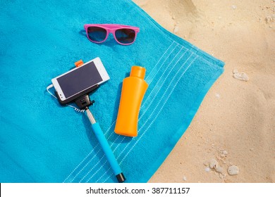 Vacation, Technology And Protection. Must Have Accessories On The Sea Beach. Smartphone, Selfie Stick, Sunscreen And Sunglasses. Top View.