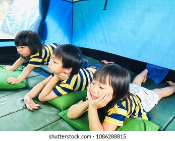 Vacation Time Concept. Happy Three Asian Kids Camping Outdoor And Lying On The Green Sleeping Cushion In The Blue Tent In The Mountain.