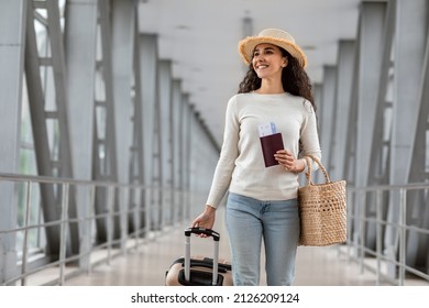 Vacation Travel. Beautiful Young Brunette Lady Wearing Wicker Hat Walking With Suitcase In Airport Terminal, Happy Smiling Millennial Lady Ready For Holiday Trip, Going To Departure Gate, Copy Space