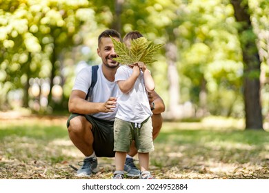 Vacation In The Woods, Family Fun In The Park, Escape To Nature And Active Weekend. A Father And Son Are Dressed In The Same Clothes. Boy Holds A Leaf In Front Of His Face While Dad Posing For A Photo