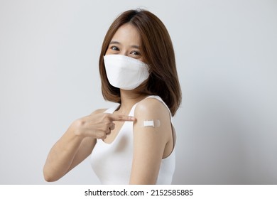 Vaccinated Asian Young Woman With Face Mask Pointing At Vaccine Shot Bandage