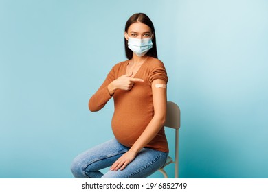 Vaccinated Pregnant Female Showing Plaster Bandage On Arm After Getting Covid-19 Vaccine Injection Sitting Wearing Protective Face Mask Over Blue Studio Background. Coronavirus Vaccination Campaign - Powered by Shutterstock