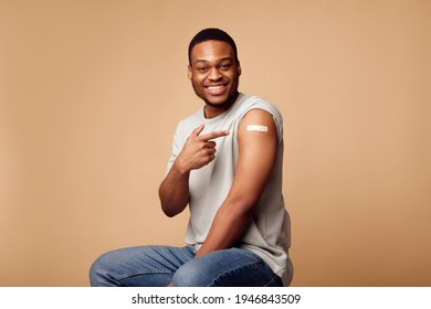 Vaccination Against Covid-19. Joyful Vaccinated African Guy Pointing Finger At Adhesive Plaster Bandage On His Arm After Coronavirus Antiviral Injection Sitting On Beige Background. I've Got Vaccine - Powered by Shutterstock