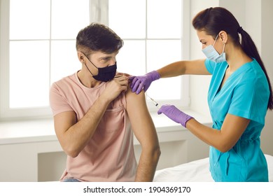Vaccination agaist covid-19 for people concept. Man patient in medical face mask sitting and getting vaccination injection with syringe against coronavirus infection from woman doctor in clinic