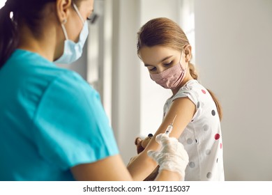 Vaccination Concept. Brave Kid In Medical Face Mask Looking At Needle While Getting Flu Shot At Doctor's Office. Nurse Injecting Little Child With Vaccine During Immunization Campaign For Children