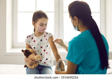 Vaccination Concept. Little Kid In Medical Face Mask Getting Covid-19 Or Flu Vaccine At Clinic. Woman Who Works As Nurse Or Doctor At Hospital Disinfects Skin On Child's Arm Before Giving Injection