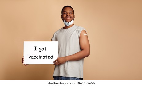 Vaccination. Happy Black Guy Holding Poster With Text I Got Vaccinated Posing Without Face Mask Showing Arm After Antiviral Vaccine Injection On Beige Studio Background. Panorama