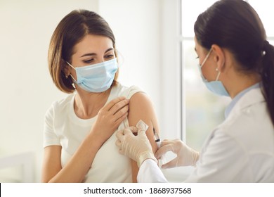 Vaccination, immunization campaign, disease prevention concept. Young woman in medical face mask getting Covid-19 vaccine at doctor's office. Professional nurse giving flu injection to patient