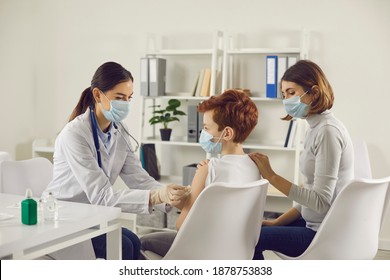 Vaccination And Immunization For Children Concept. Child Getting Injection At The Hospital And Mom Supporting Him. Nurse Or Doctor In Medical Face Mask Giving Flu Or Covid-19 Vaccine To Little Boy