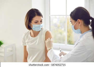 Vaccination, immunization, disease prevention concept. Doctor disinfects skin on patient's arm before giving injection. Young woman in medical face mask getting Covid-19 or flu vaccine at the clinic