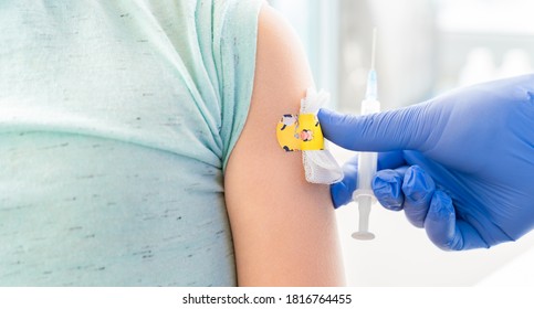 Vaccination of little girl in doctor's office. Kids funny adhesive plaster. Syringe with vaccine for covid-19 coronavirus,flu,dangerous infectious diseases. Injection. Clinical trials for human,child.