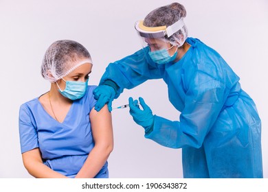 Vaccination Of Medical Personal. A Doctor In Protective Gear, A Medical Mask And A Screen Gives Another Female Doctor A Vaccine For Covid 19. Priority Group For Immunization