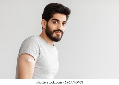 Vaccination Of Population And Protection Of Health From Covid-19 Virus, Medical Service. Friendly Attractive Arabian Young Bearded Man Showing Shoulder With Band Aid After Shot, On Gray Background