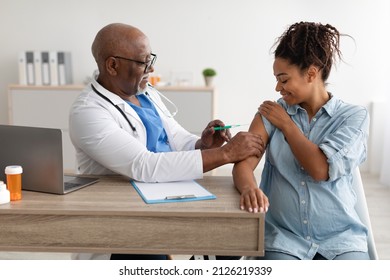 Vaccination In Pregnancy. Smiling Pregnant Young Black Woman Getting Vaccinated At Clinic, Mature Male Doctor In Glasses Giving Vaccine Shot Injecting Mother-To-Be In Arm. Covid-19 And Flu Prevention - Powered by Shutterstock