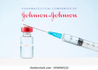 A vaccination syringe and a glass ampoule with a clear liquid on a blue background with the logo of a pharmaceutical company Johnson and Johnson. March 13, Barnaul, Russia.