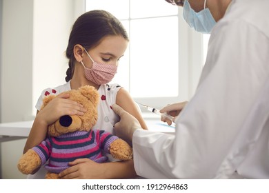 Vaccine against coronavirus for kids during outbreak concept. Little girl patient in medical protective mask with toy sitting getting vaccination injection with syringe against covid-19 from doctor - Powered by Shutterstock - Get 15% off with code: PIKWIZARD15